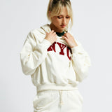 Person wearing a white hoodie and shorts with 'NYC' text on a plain background