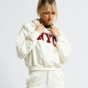 Person wearing a white hoodie and shorts with 'NYC' text on a plain background