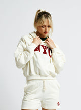 Person wearing a white hoodie and shorts with 'NYC' text on a plain background